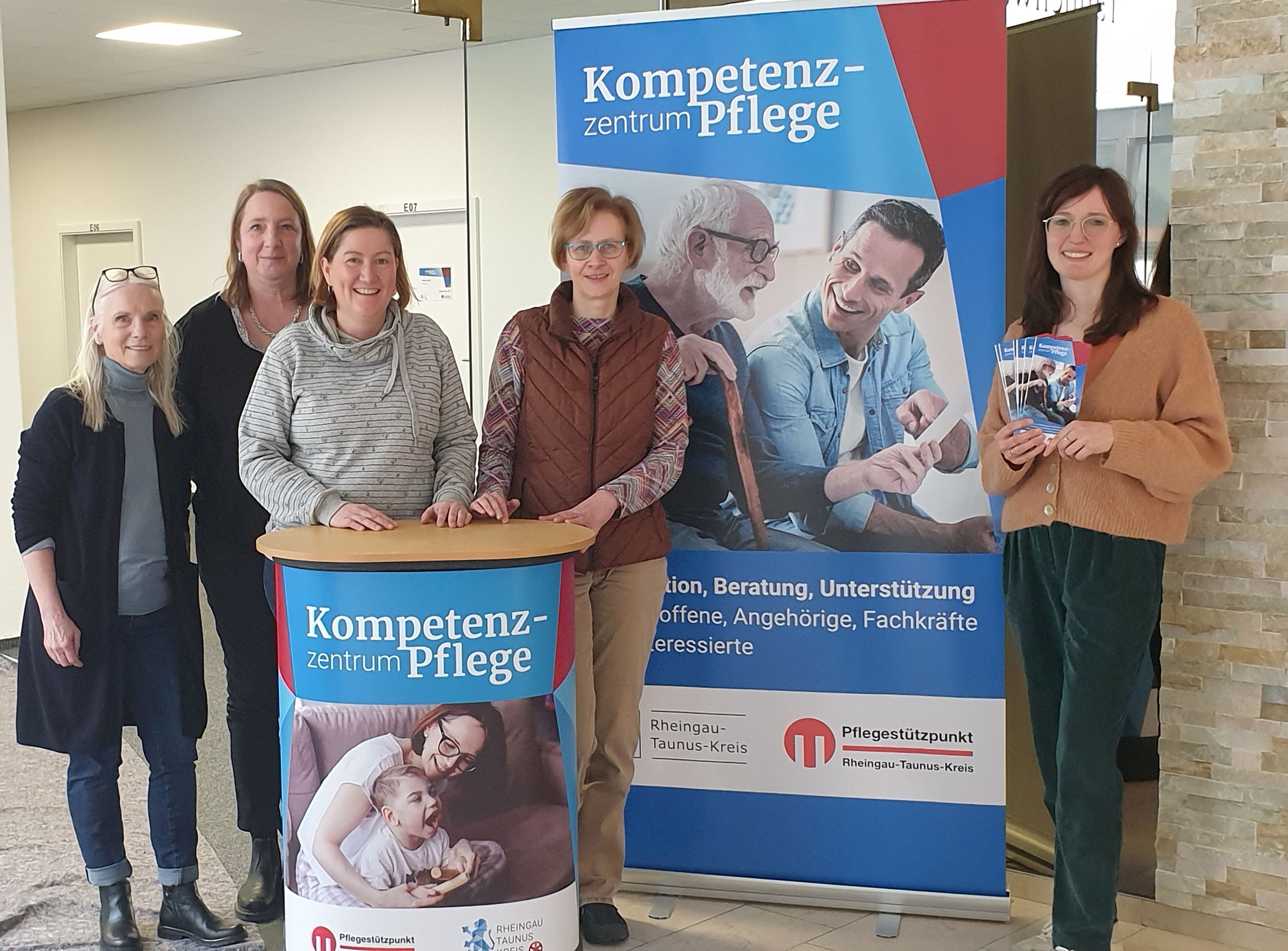 Bild: Das Team des Kompetenzzentrums Pflege des Rheingau-Taunus-Kreises steht vor einem Veranstaltungsplakat.